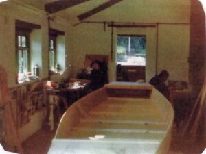 A boat inside the Triangle boat workshop with David Vause sitting in the corner