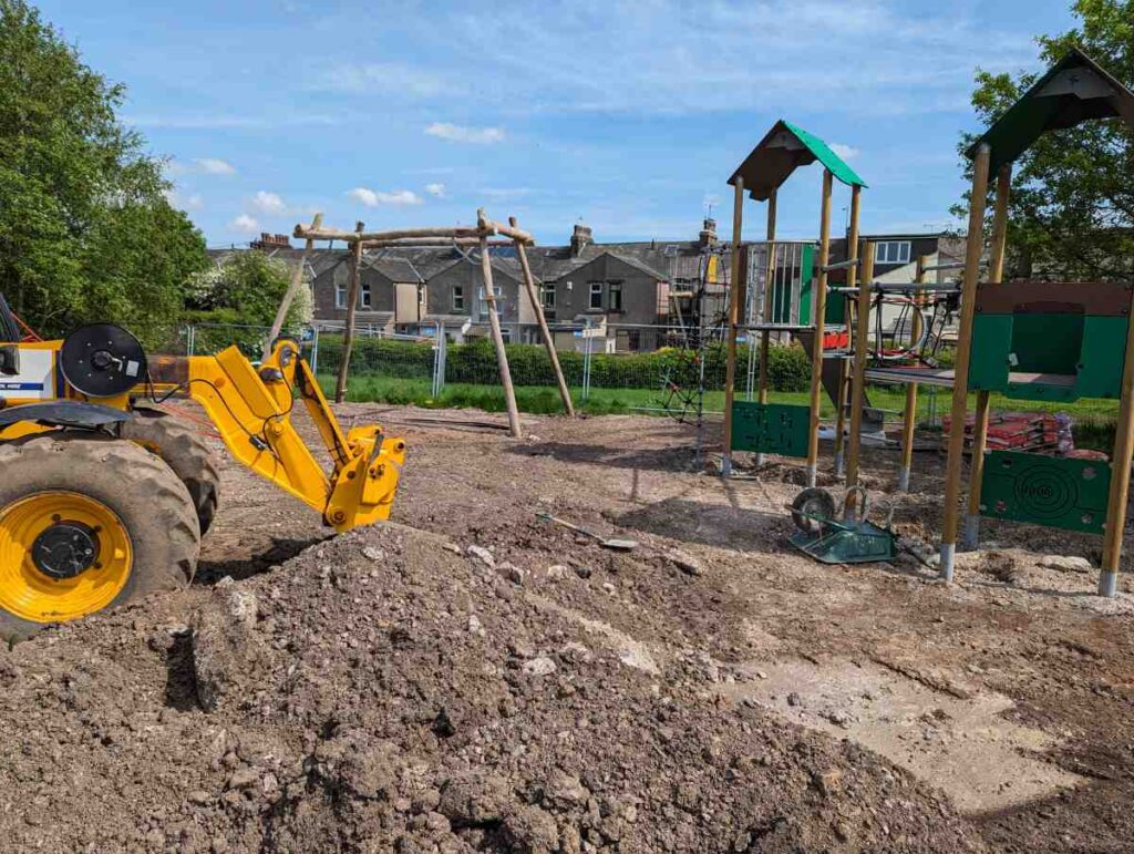 Playground with all earth dug up and a digger in the foreground